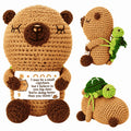 Crocheted teddy bear with a message card and a small green creature on a white background
