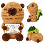 Crocheted teddy bear with a message card and a small green creature on a white background