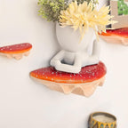 Decorative wall shelves with a sitting figure and plants on a white wall.
