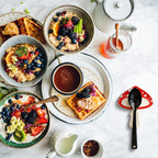 Breakfast spread with bowls of oatmeal, waffles, and a cup of coffee on a marble surface.