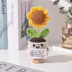 Crocheted sunflower plant with a motivational message on a surface.