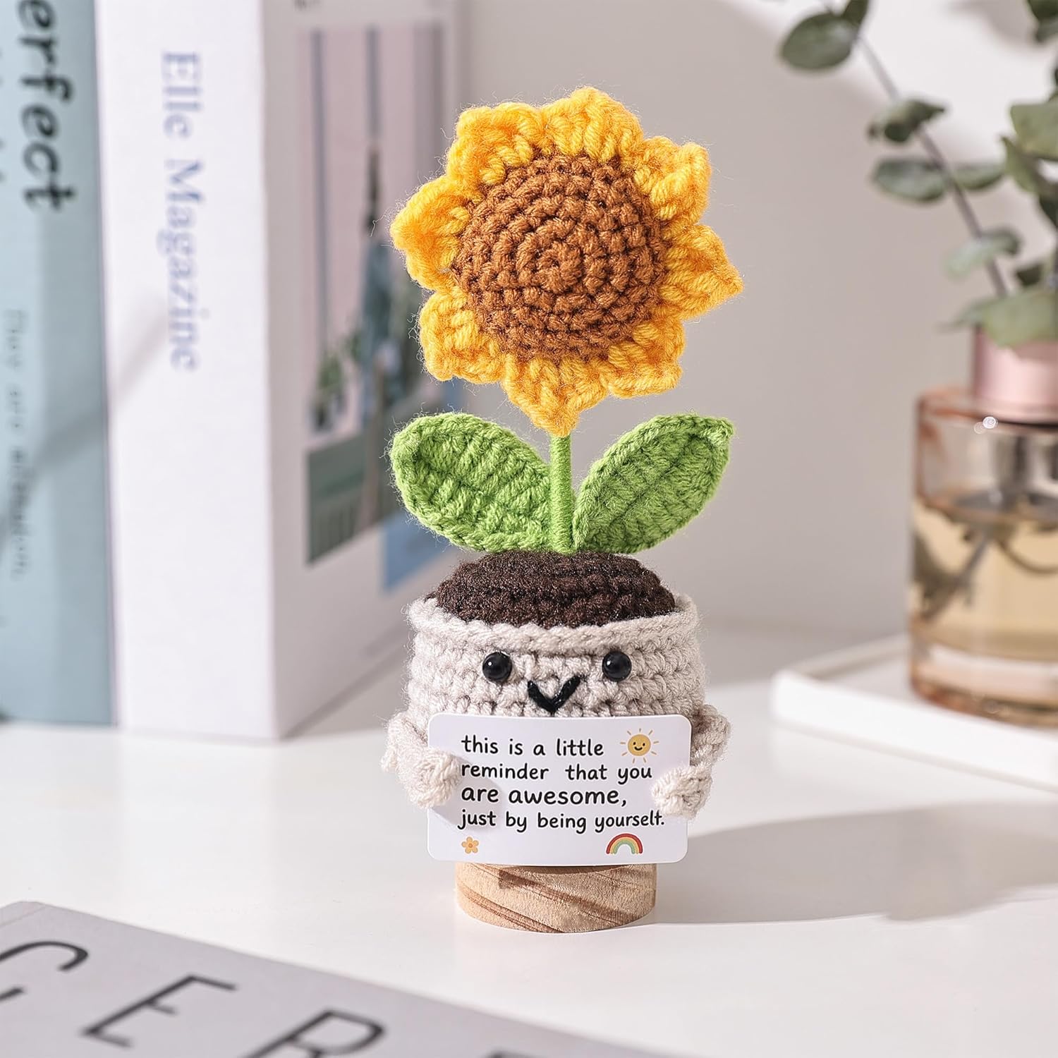 Crocheted sunflower plant with a motivational message on a surface.